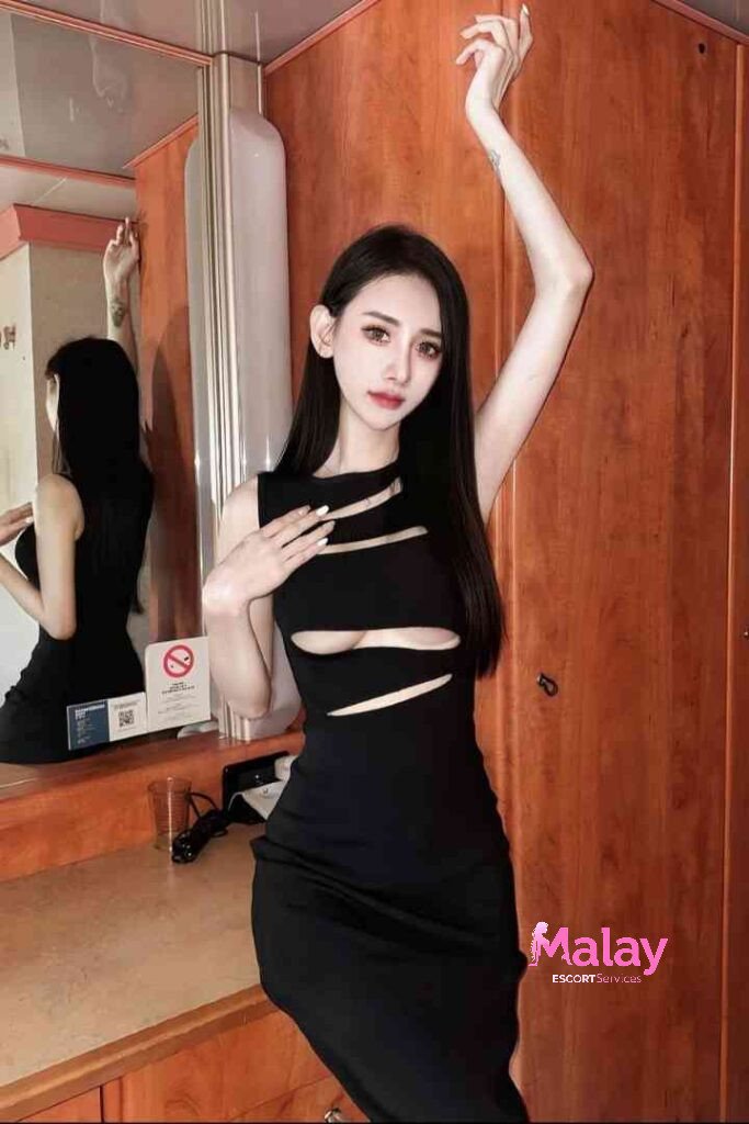 Malay Escort Service Woman in a black cutout dress posing with arms raised standing in a room with wooden paneling KL Escort Girl Malay Escort KL Real KL Escorts Ready for You Malay Escort Service Woman in a black cutout dress posing with arms raised standing in a room with wooden paneling KL Escort Girl