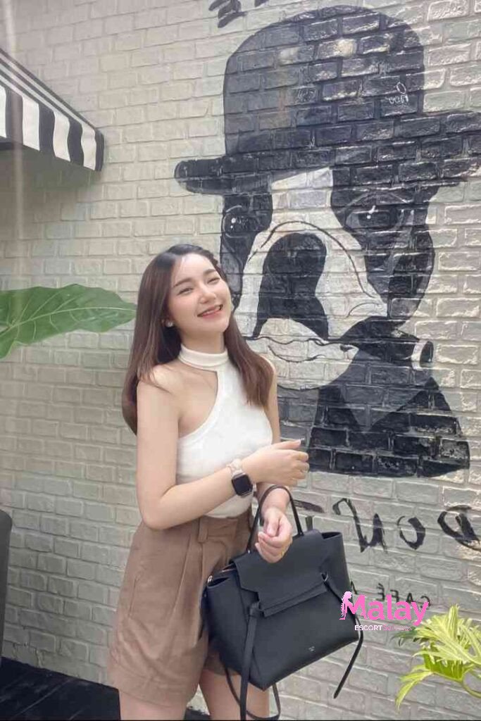 Malay Escort Service Smiling woman with a white top brown skirt and black bag standing outside KL Escort Girl