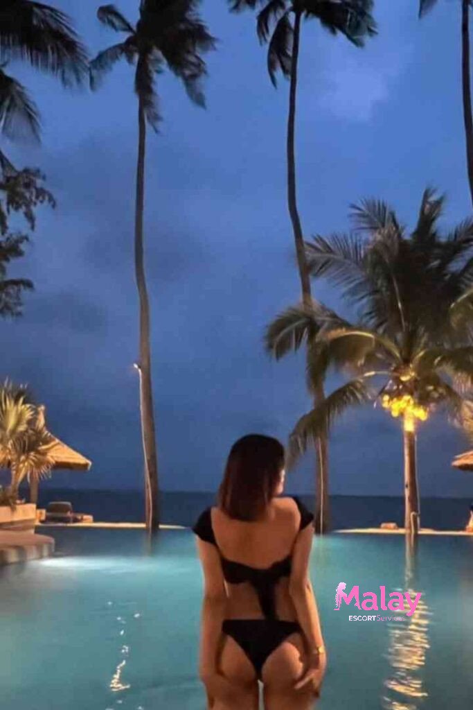Malay Escort Service Woman in black bikini by pool at night with palm trees KL Escort Girl