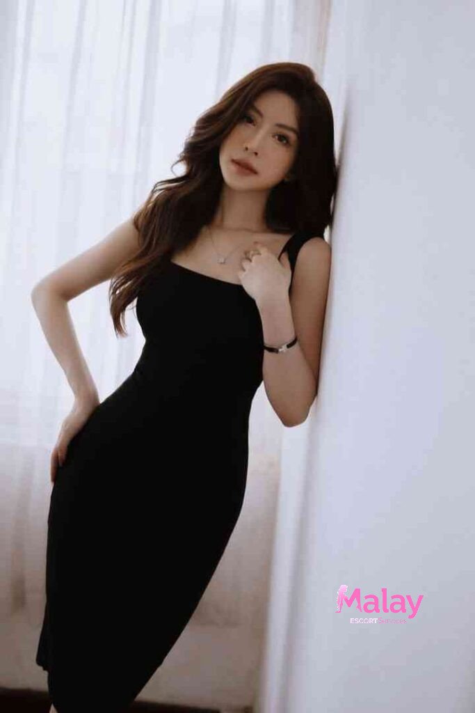 Malay Escort Service Elegant woman in a black dress leans against a white wall KL Escort Girl Malay Escort KL Real KL Escorts Ready for You Malay Escort Service Elegant woman in a black dress leans against a white wall KL Escort Girl