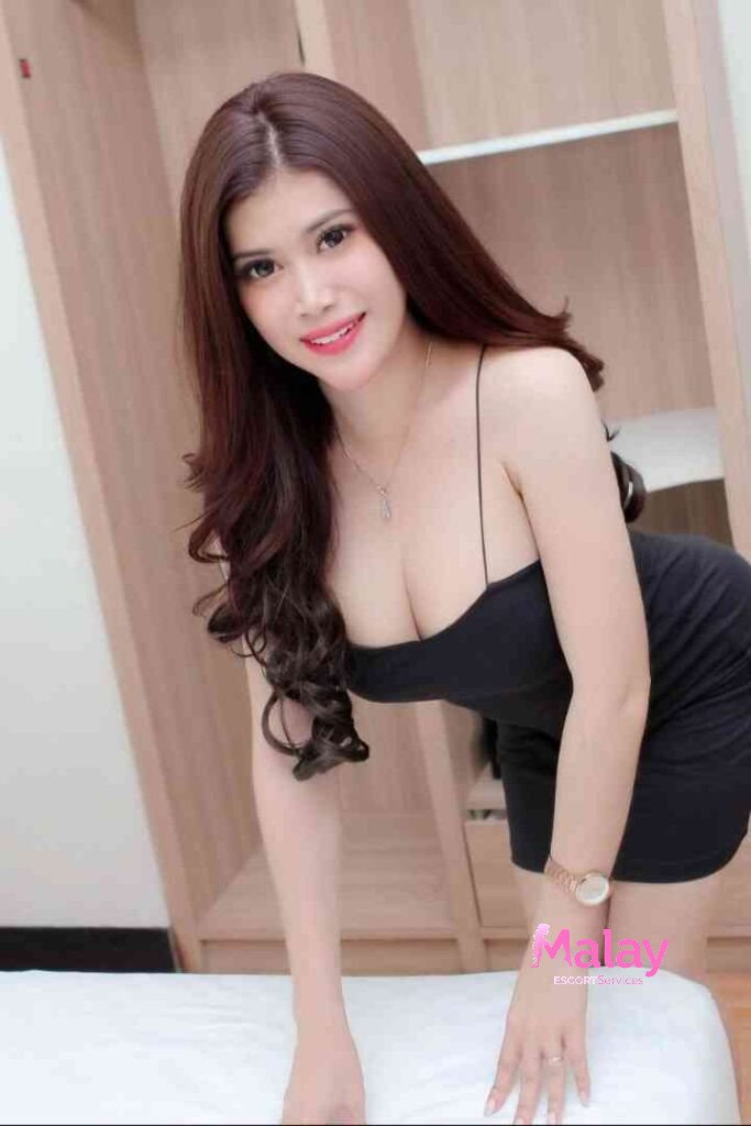 Malay Escort Service Young woman in a black dress leans forward smiling at the camera KL Escort Girl