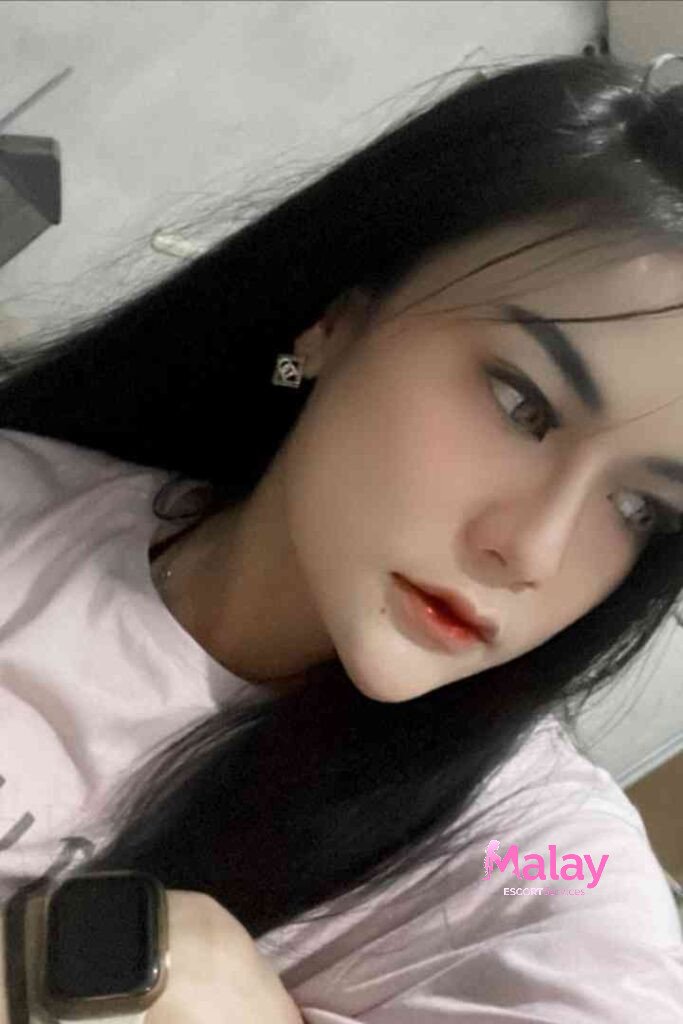 Malay Escort Service Young woman with long black hair and subtle makeup wearing a pink t shirt and earrings KL Escort Girl