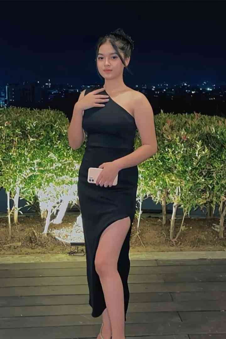 Malay Escort Service Young woman in a black one-shoulder dress with a thigh-high slit holding a phone. KL Escort Girl