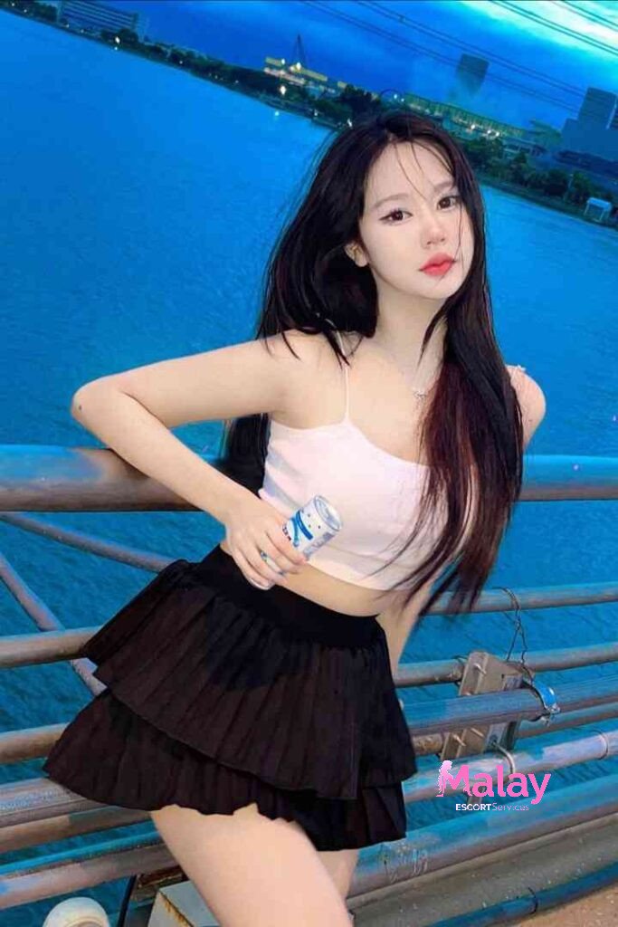 Malay Escort Service Young woman in a white crop top and black pleated skirt holding a drink by a railing at night KL Escort Girl Malay Escort KL Real KL Escorts Ready for You Malay Escort Service Young woman in a white crop top and black pleated skirt holding a drink by a railing at night KL Escort Girl