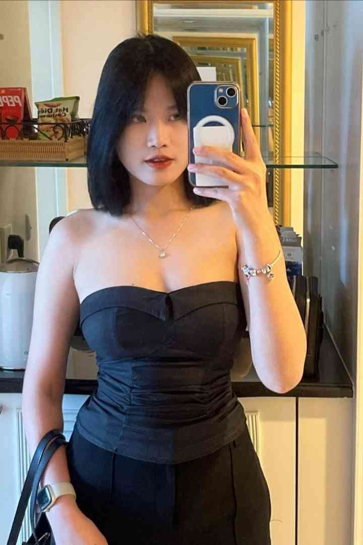 Malay Escort Service Young woman in a black strapless top takes a mirror selfie with a smartphone. KL Escort Girl