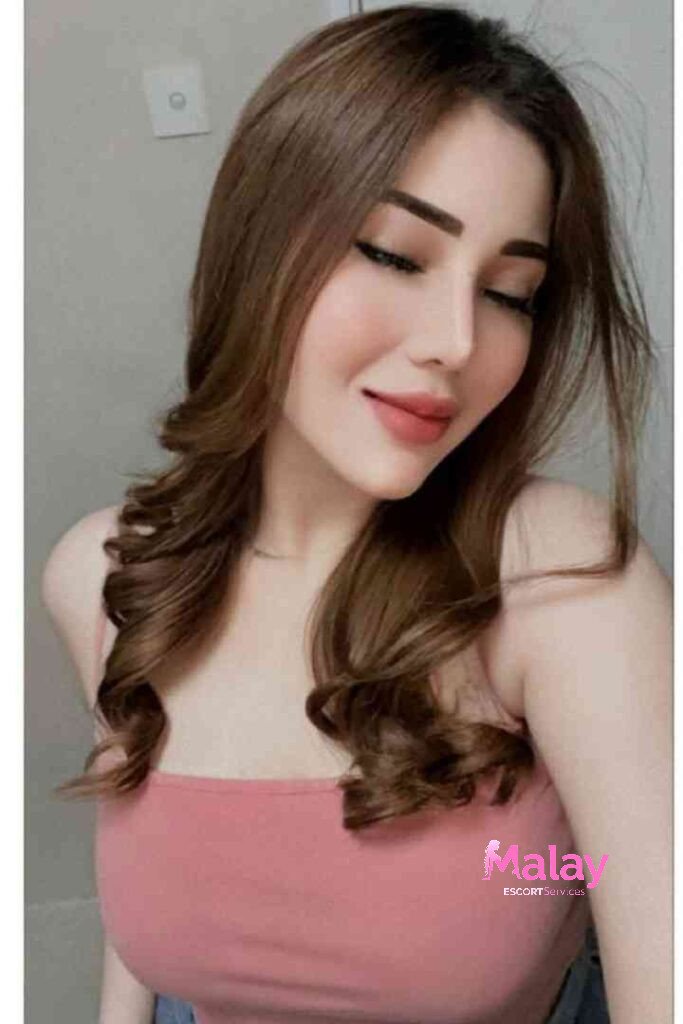 Malay Escort Service Young woman with brown wavy hair and pink top looking down with eyes closed KL Escort Girl