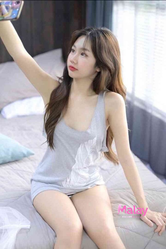 Malay Escort Service Young woman in a grey tank top taking a selfie while sitting on a bed KL Escort Girl Malay Escort KL Real KL Escorts Ready for You Malay Escort Service Young woman in a grey tank top taking a selfie while sitting on a bed KL Escort Girl