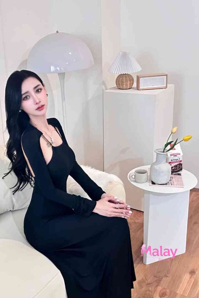 Malay Escort Service Woman in a long black dress with an open back sits on a couch KL Escort Girl Malay Escort KL Real KL Escorts Ready for You Malay Escort Service Woman in a long black dress with an open back sits on a couch KL Escort Girl