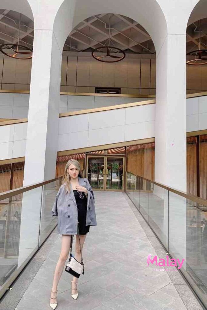 Malay Escort Service Woman in a gray pinstripe blazer and black dress poses on a modern walkway KL Escort Girl