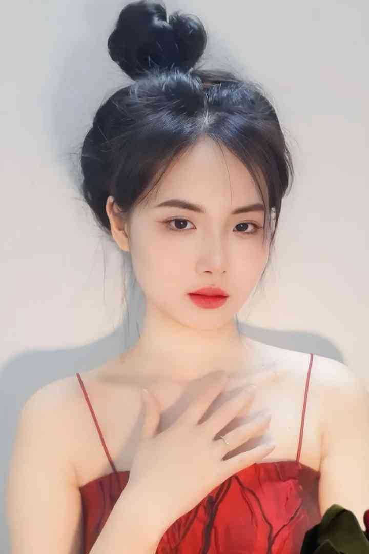 Malay Escort Service Young woman with dark hair in a bun, wearing a red spaghetti strap dress, with her hand on her chest. KL Escort Girl