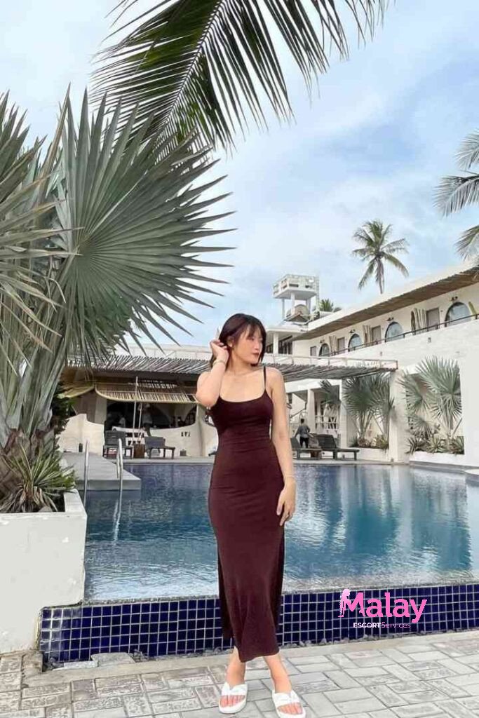 Malay Escort Service Woman in a brown midi dress by a resort pool with palm trees KL Escort Girl