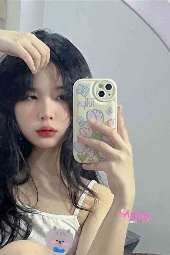 Malay Escort Service Young woman with dark hair taking a selfie with a phone featuring a floral design KL Escort Girl Malay Escort KL Real KL Escorts Ready for You Malay Escort Service Young woman with dark hair taking a selfie with a phone featuring a floral design KL Escort Girl