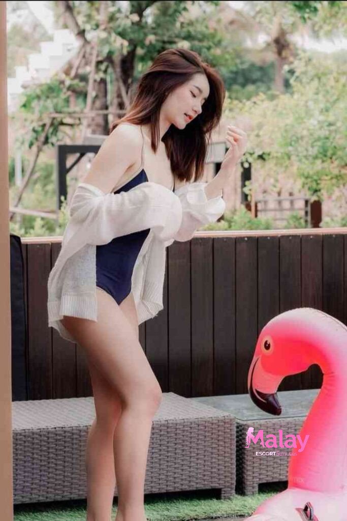 Malay Escort Service Woman in swimsuit and white cardigan poses by a pool with a pink flamingo float KL Escort Girl