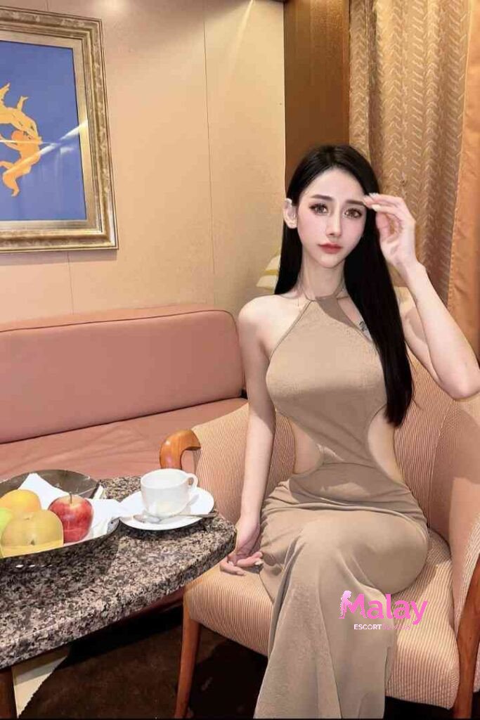 Malay Escort Service Woman in a tan cutout dress sits in a chair with fruit and coffee on a table KL Escort Girl Malay Escort KL Real KL Escorts Ready for You Malay Escort Service Woman in a tan cutout dress sits in a chair with fruit and coffee on a table KL Escort Girl