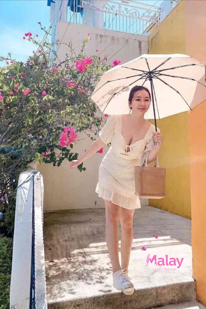 Malay Escort Service Woman in white dress holding umbrella and purse standing on steps with pink flowers KL Escort Girl Malay Escort KL Real KL Escorts Ready for You Malay Escort Service Woman in white dress holding umbrella and purse standing on steps with pink flowers KL Escort Girl