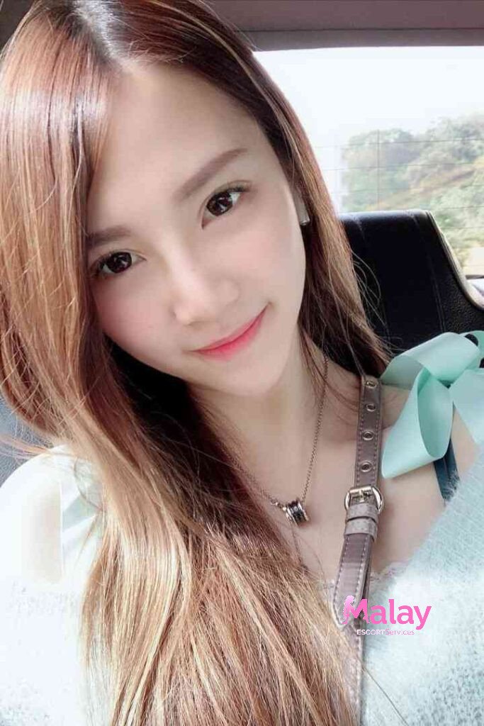 Malay Escort Service Young woman with long brown hair and a light blue top smiles at the camera KL Escort Girl