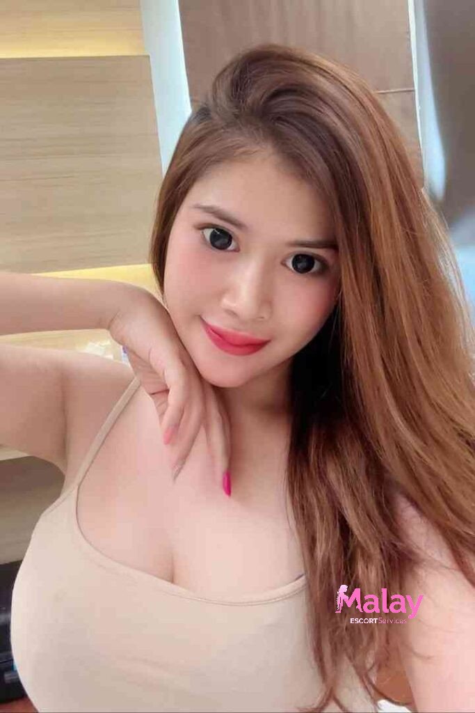 Malay Escort Service Young woman with long brown hair and bright makeup smiles at the camera KL Escort Girl