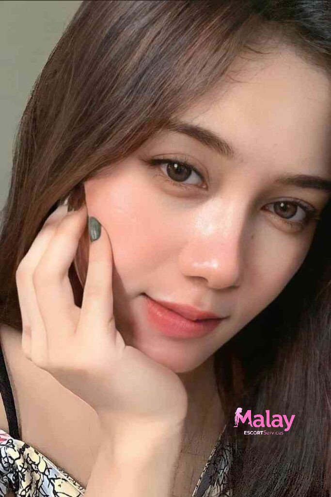 Malay Escort Service Close up of a young woman with brown hair and brown eyes touching her cheek KL Escort Girl