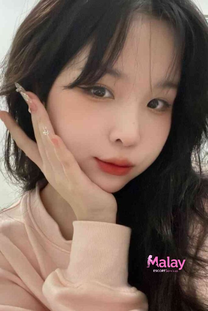 Malay Escort Service Young woman with dark hair and bangs wearing a pink sweatshirt touches her face with her hand KL Escort Girl Malay Escort KL Real KL Escorts Ready for You Malay Escort Service Young woman with dark hair and bangs wearing a pink sweatshirt touches her face with her hand KL Escort Girl