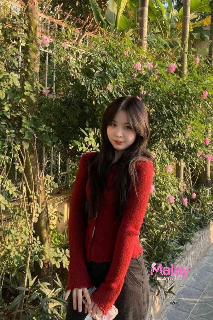 Malay Escort Service Young woman in a red sweater smiles in front of a floral backdrop KL Escort Girl Malay Escort KL Real KL Escorts Ready for You Malay Escort Service Young woman in a red sweater smiles in front of a floral backdrop KL Escort Girl