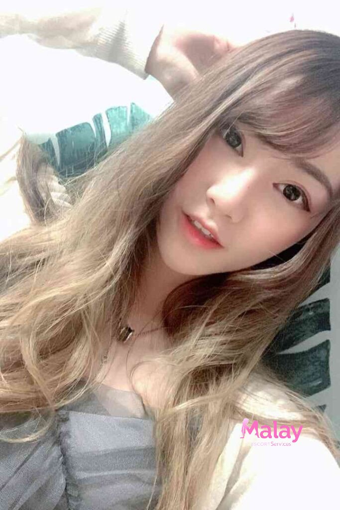 Malay Escort Service Young woman with long wavy brown hair and bangs looking at the camera with a gentle smile KL Escort Girl